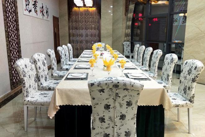 A long dining table with floral-patterned chairs, set with white tablecloths, plates, and yellow flowers.