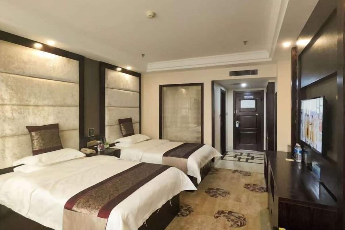 A hotel room with two beds, a television, and a carpeted floor.