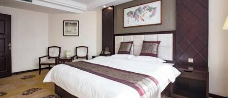 A hotel room with a large bed, a headboard with a decorative panel, a framed artwork above the bed, and a carpet with a pattern.