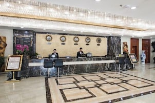 Zona de recepción de un hotel con mostrador de mármol, dos recepcionistas y una pared decorativa.