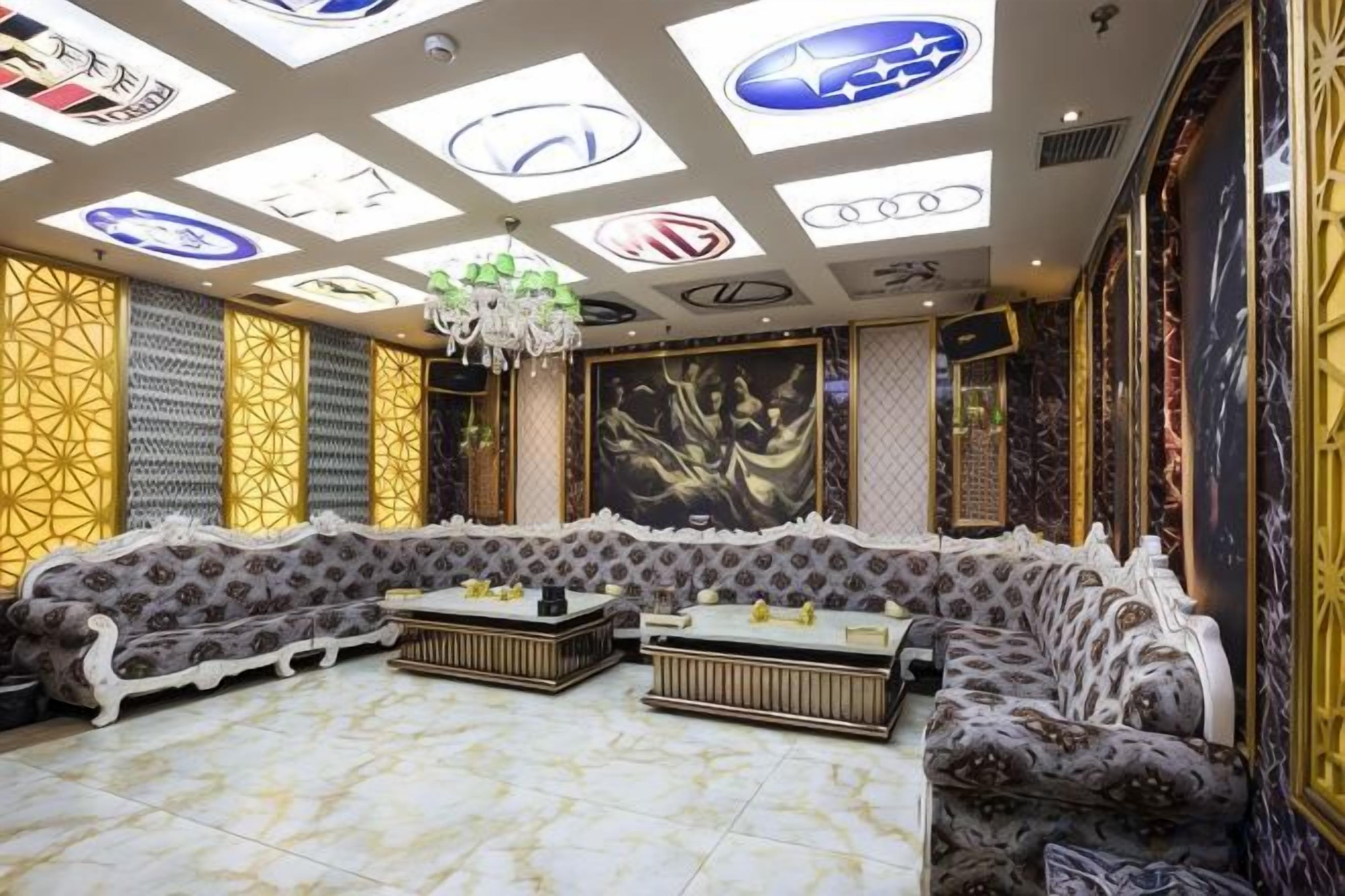 A luxurious lounge with a patterned sofa set, a chandelier, and a large wall mural.