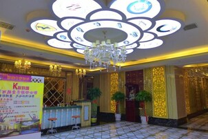 A hotel lobby with a chandelier, reception desk, and potted plants.