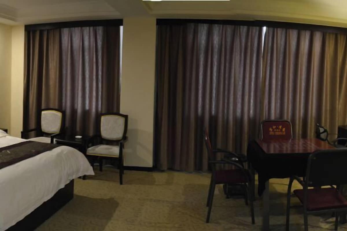 A hotel room with a bed, a desk, and a chair. There are curtains on the windows.