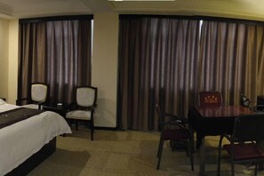 A hotel room with a bed, a desk, and a chair. There are curtains on the windows. - Xiyan International Hotel (Huining)