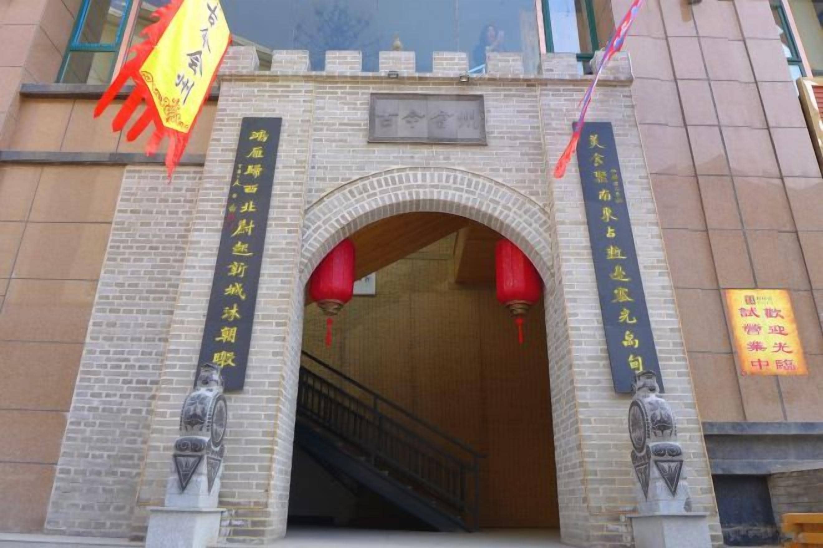 Entrada de edificio con arco de ladrillo, una escalera que baja y dos faroles rojos.