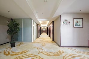 A hotel hallway with a patterned carpet, a potted plant, and a sign on the wall. - Xiyan International Hotel (Huining)