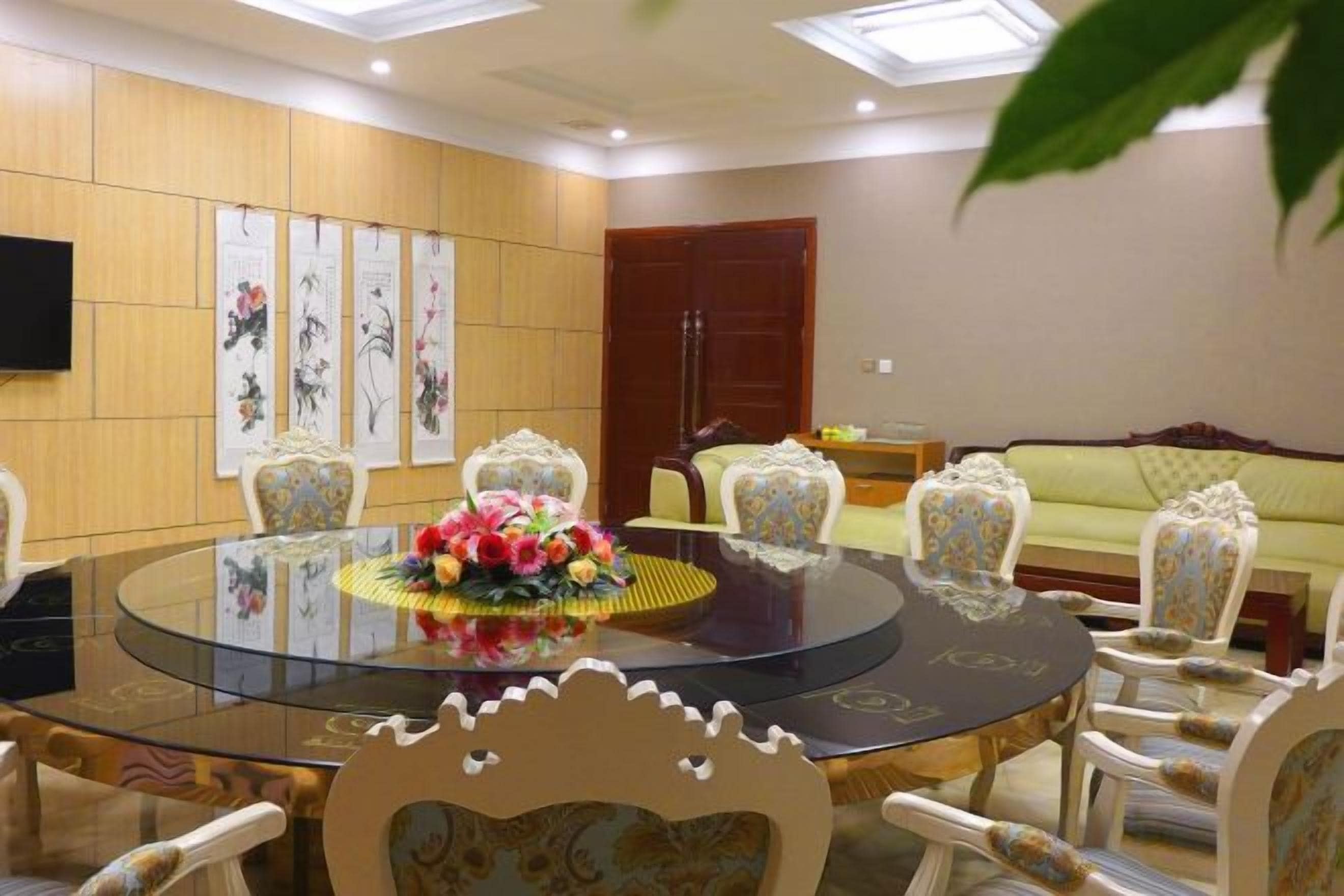 A conference room with a round glass table, white ornate chairs, a sofa, and a television on the wall.