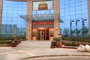 A hotel entrance with a glass facade, a red sign above the doors, and a reflection of buildings in the windows. - Xiyan International Hotel (Huining)