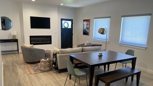 Una sala de estar moderna con un sofá, una mesa de comedor y un televisor montado en la pared.