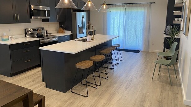 Una cocina moderna con armarios oscuros, electrodomésticos de acero inoxidable, una isla grande con taburetes e iluminación colgante.