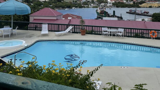 Ein Swimmingpool mit Liegestühlen und Sonnenschirmen mit Blick auf ein Gewässer, im Hintergrund Boote und Gebäude.