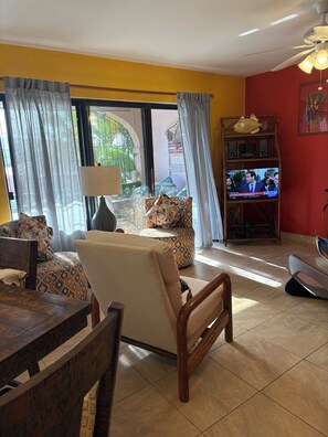 Un salon avec un canapé, des fauteuils, un téléviseur et un ventilateur de plafond.
