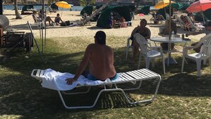 Eine Strandansicht mit badenden Personen, Palmen und Strandsonnenschirmen.