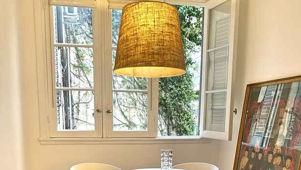 A dining area with a round table, four white chairs, a hanging lamp, and a framed picture on the wall. - Beautiful apartment in the heart of Buenos Aires Art (CABA)