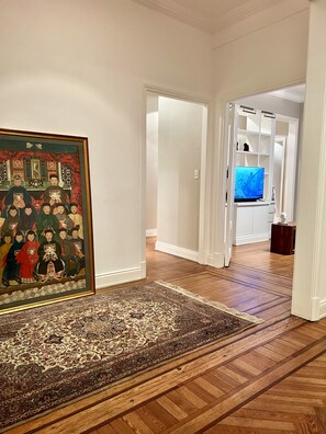 Um corredor com piso de madeira, um quadro emoldurado e uma televisão ao fundo.