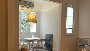 A modern living room with a beige armchair, a glass coffee table, and a dining area with a white table and chairs. - Beautiful apartment in the heart of Buenos Aires Art (CABA)