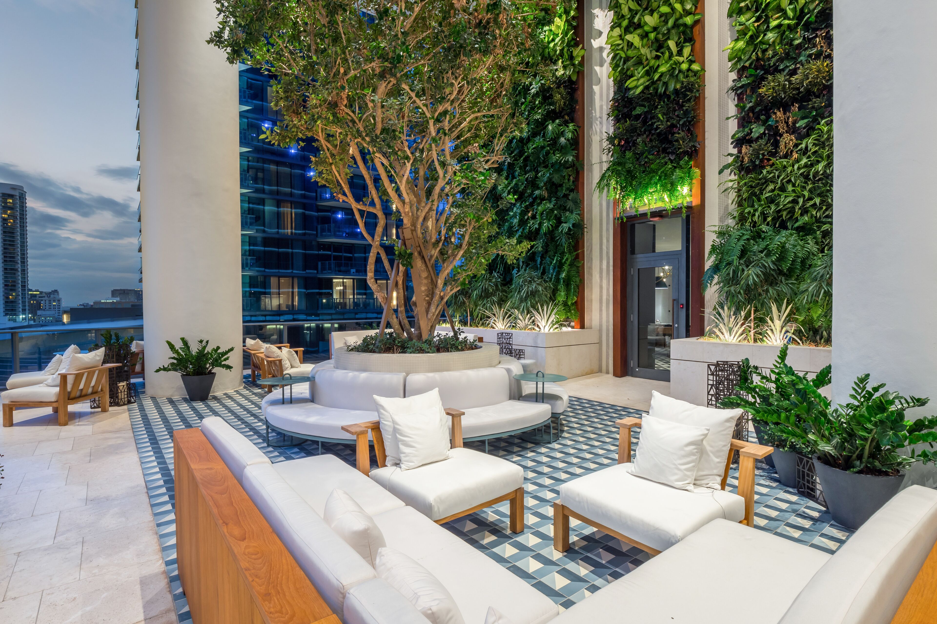 A rooftop lounge with a large tree, white sofas, and a patterned floor.
