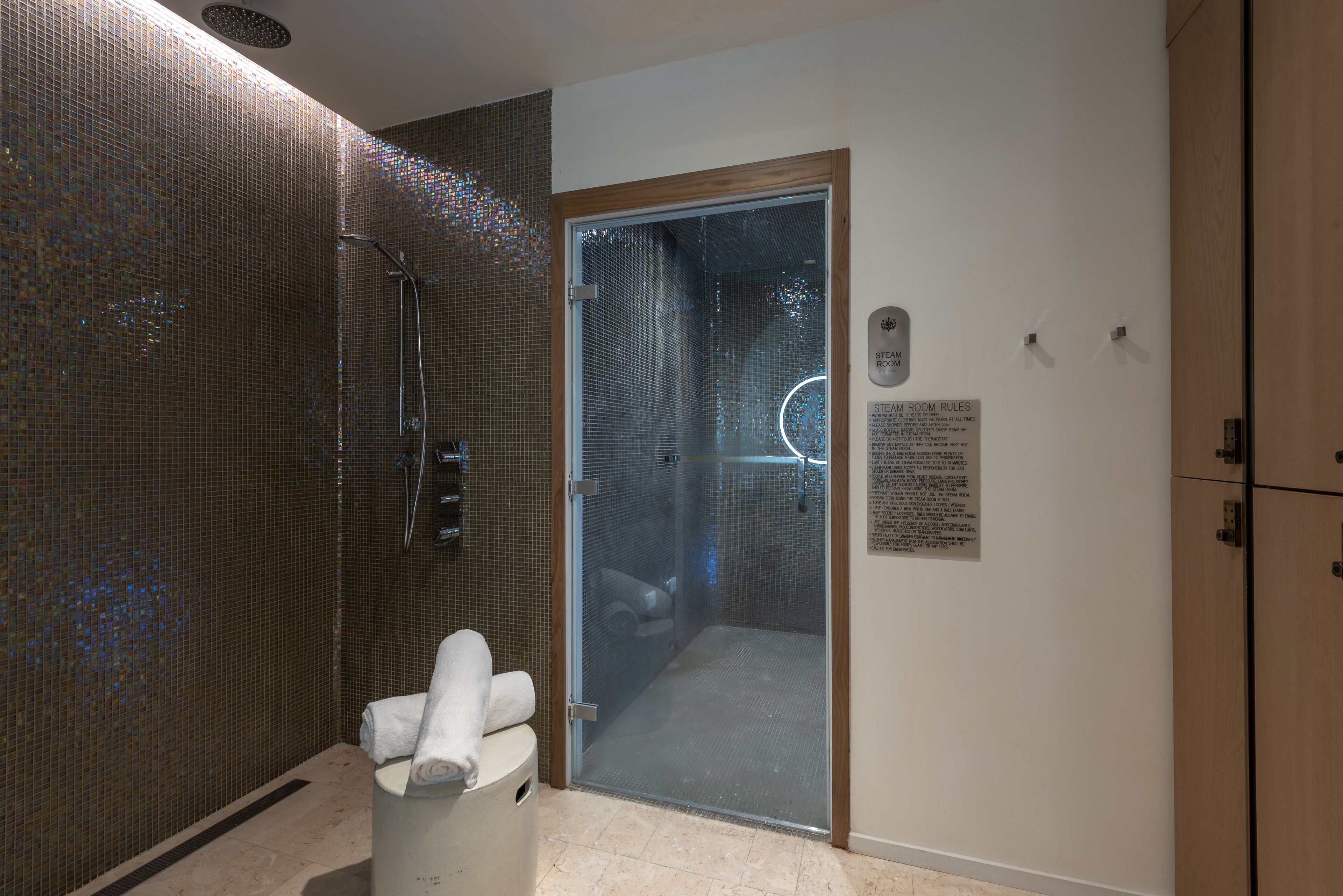 A modern shower area with a glass door, a towel rack, and a sign indicating steam room rules.