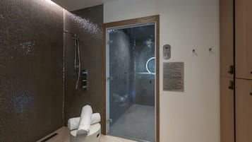 A modern shower area with a glass door, a towel rack, and a sign indicating steam room rules.