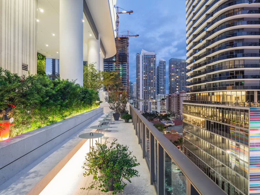 Una azotea urbana moderna con barandilla de vidrio, áreas verdes y vistas de edificios altos aledaños.