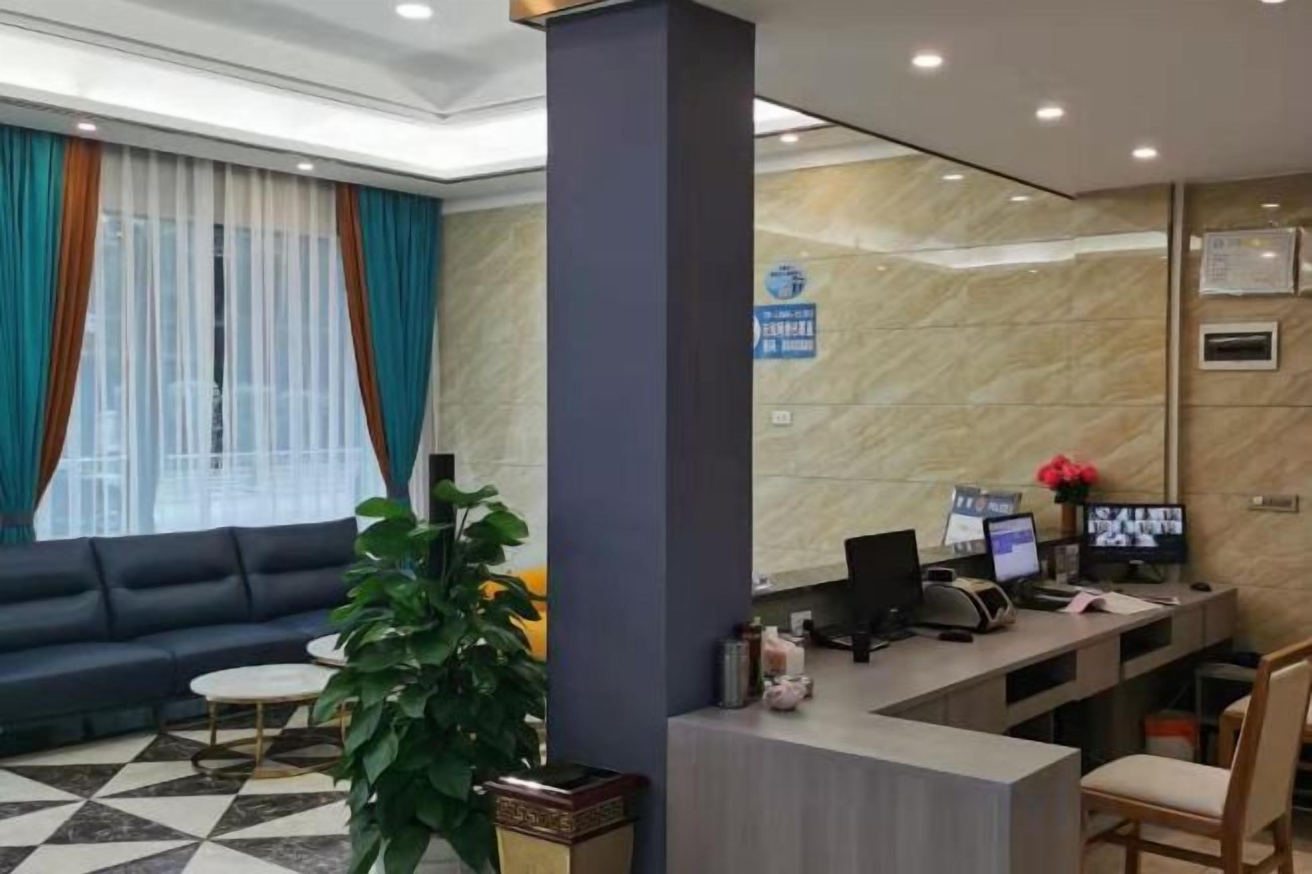 Zona de recepción de un hotel con un sofá, un mostrador, una computadora y una planta.