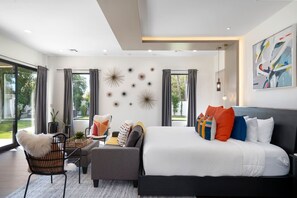 A modern bedroom with a large bed, a sofa, a chair, and a dining table.