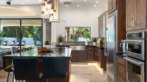 A modern kitchen with a large island, stainless steel appliances, and a view of a pool. - Resort-Style Escape with Heatable Pool, Games & Modern Design (Scottsdale)