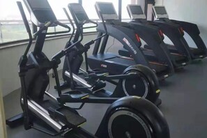 Række stillastående cykler i et fitnesscenter med udsigt fra et vindue.