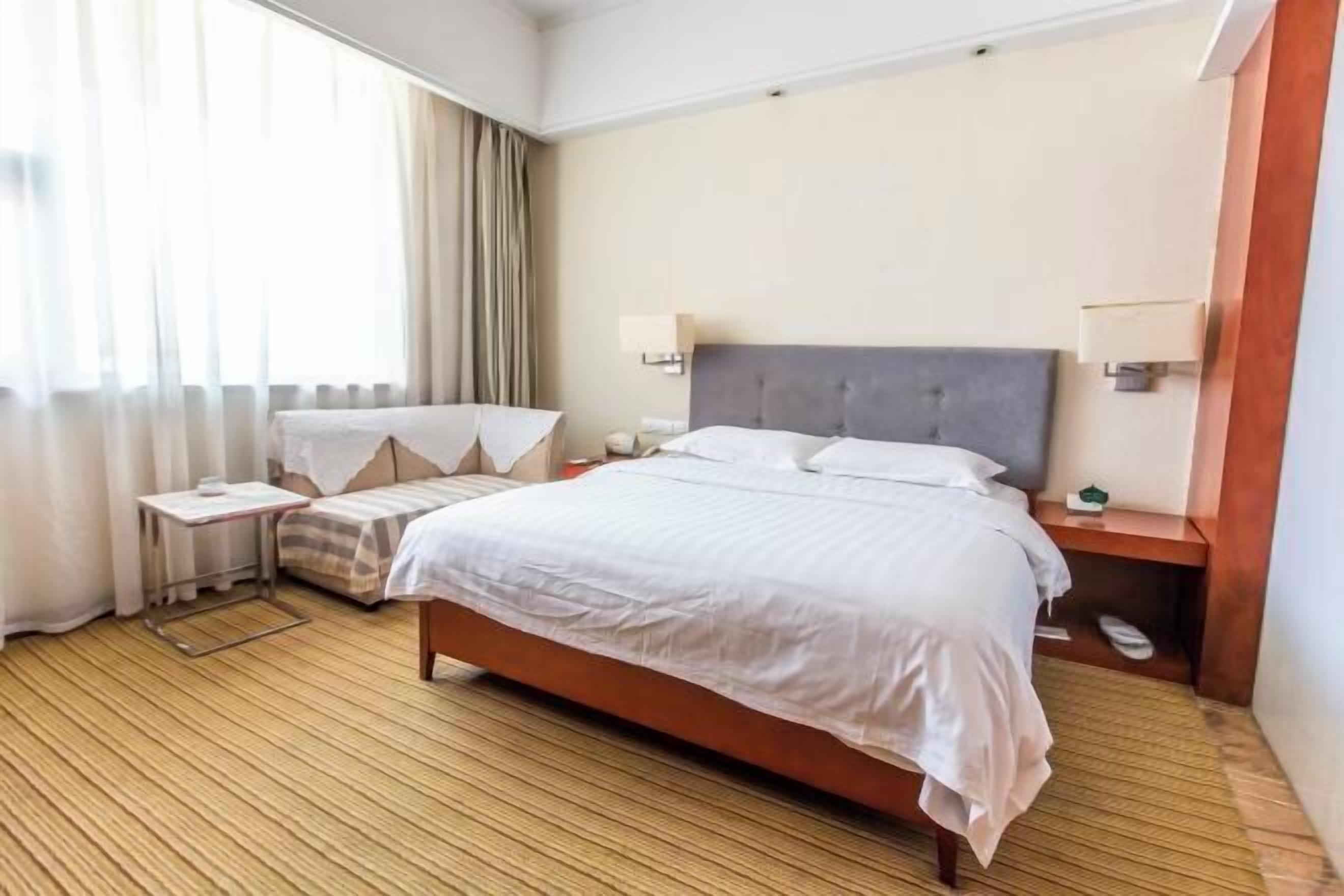 A hotel room with a bed, bedside tables, a nightstand, a lamp, and a window with curtains.