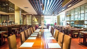 A modern restaurant with long wooden tables and leather chairs, featuring a contemporary design with a striped ceiling and large windows. - University Hotel (Binzhou)