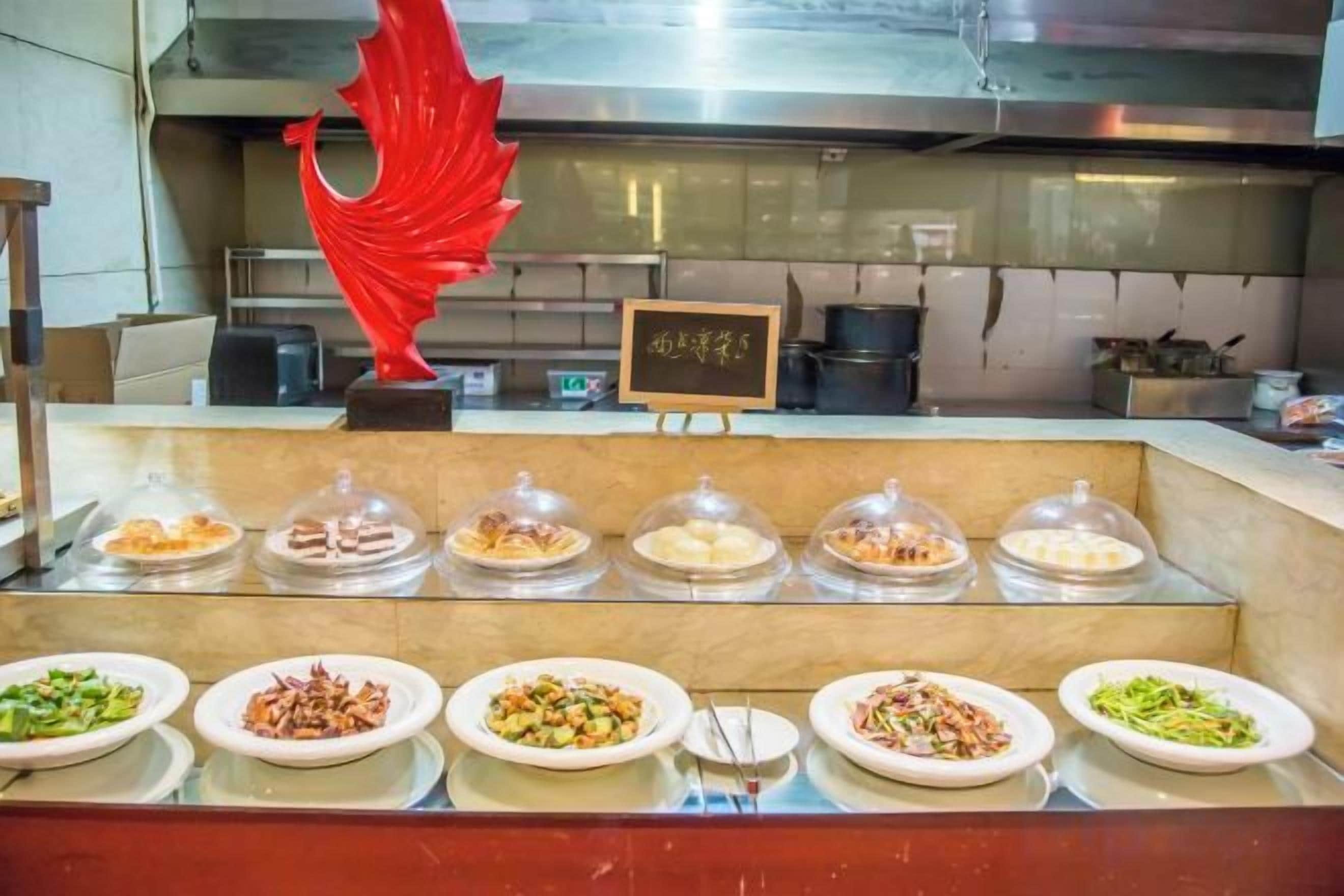 Un banco buffet con diversi piatti coperti da cupole di vetro, una scultura decorativa rossa e un cartello con caratteri giapponesi.