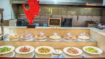 Un banco buffet con diversi piatti coperti da cupole di vetro, una scultura decorativa rossa e un cartello con caratteri giapponesi.