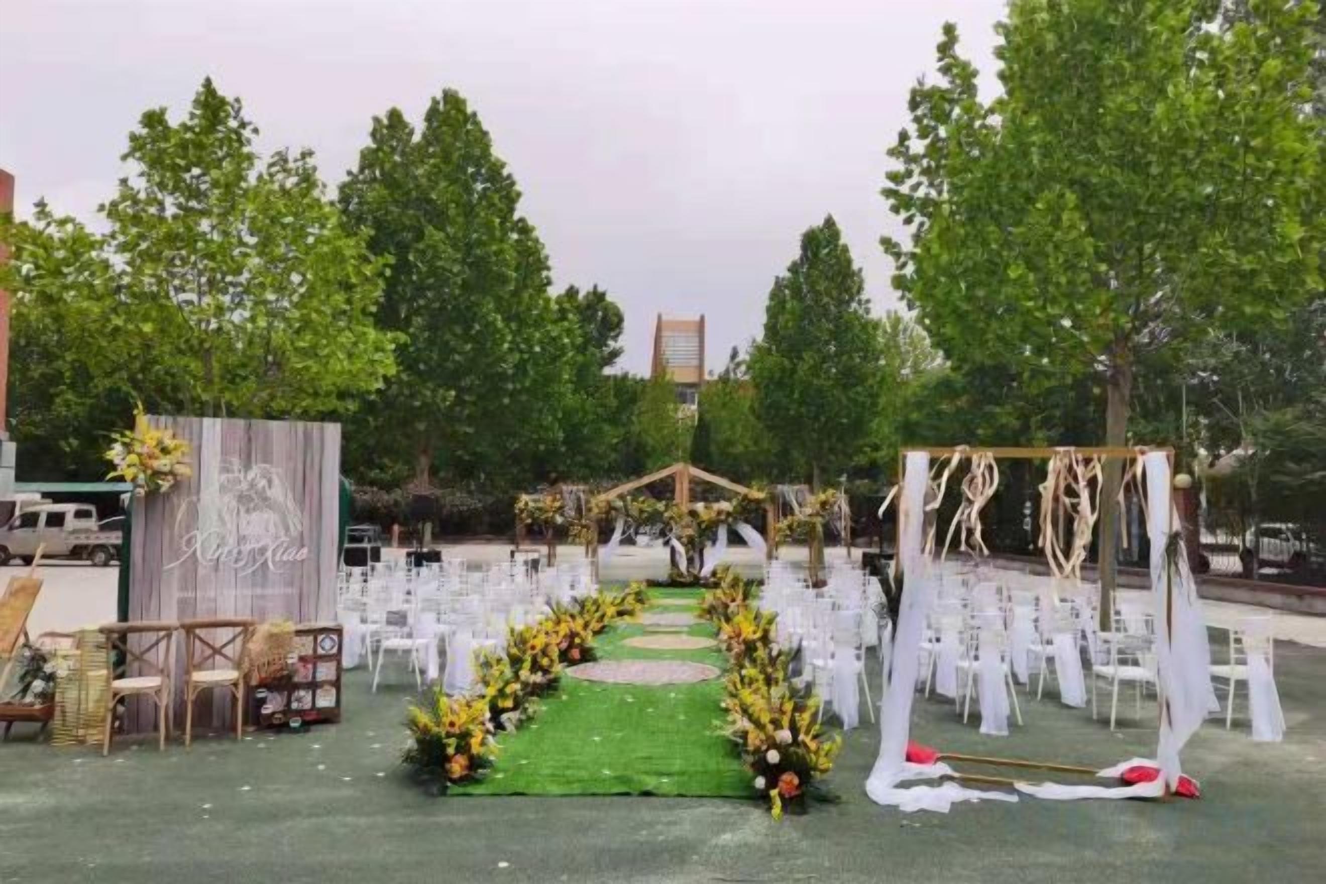 Location per matrimonio all'aperto con un corridoio rivestito di tappeto verde, sedie bianche e decorazioni floreali.