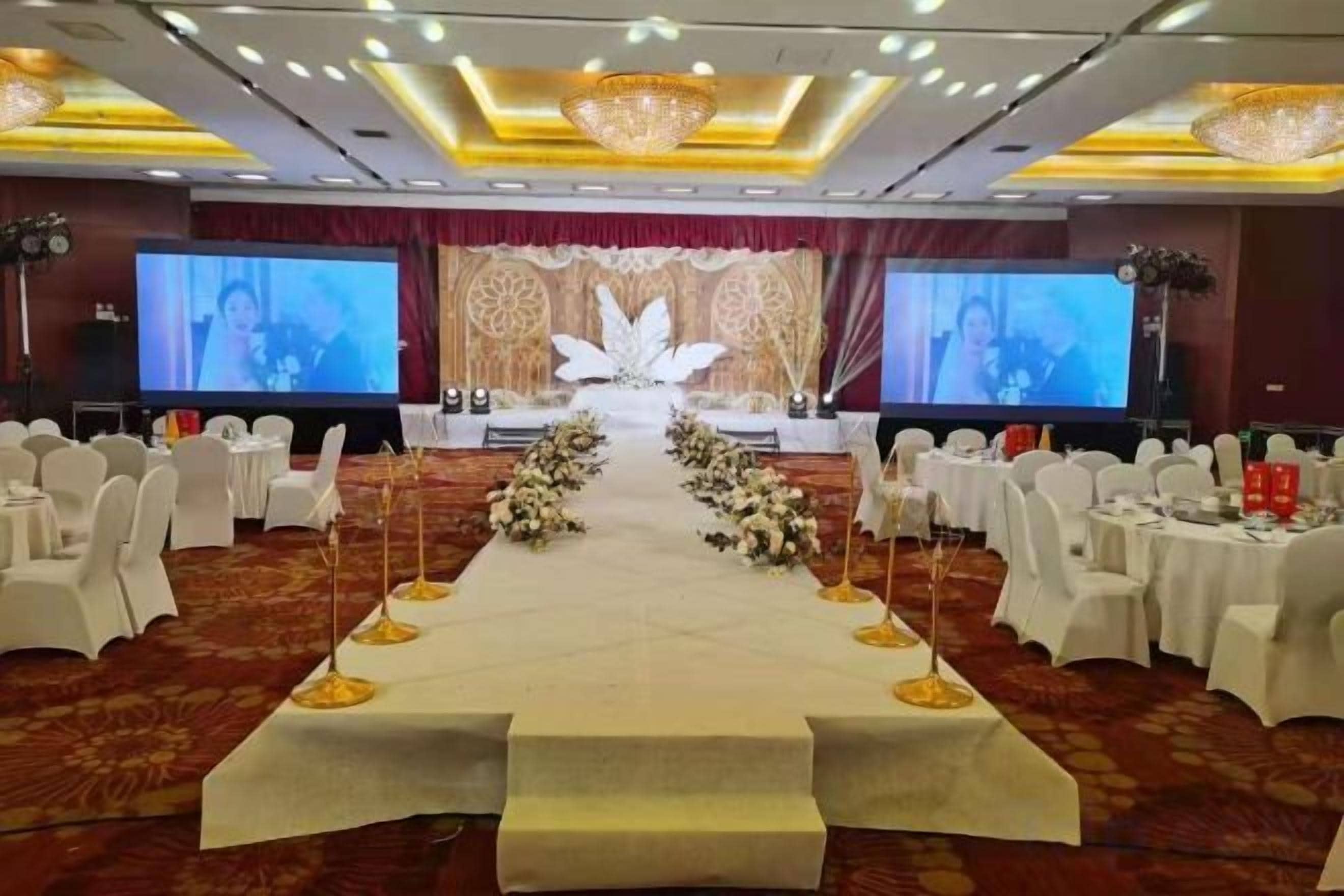 A banquet hall with a stage, rows of white chairs, and floral centerpieces.