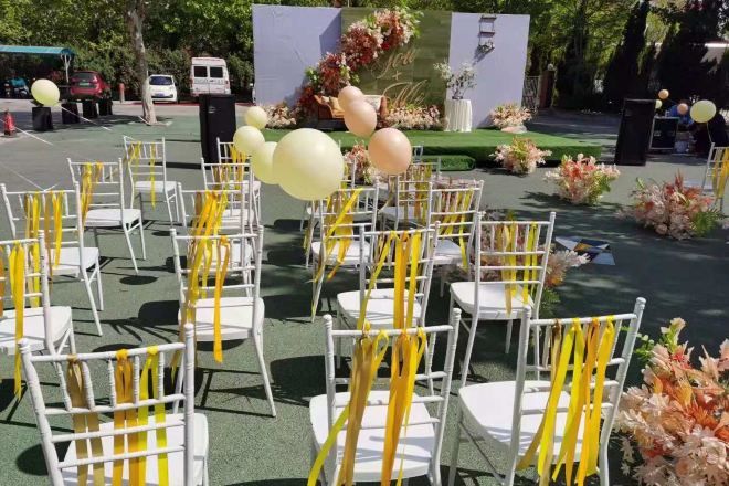 Rows of white chairs with yellow sashes, arranged in an outdoor setting with a stage and floral decorations.