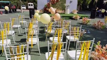 Rows of white chairs with yellow sashes, arranged in an outdoor setting with a stage and floral decorations.