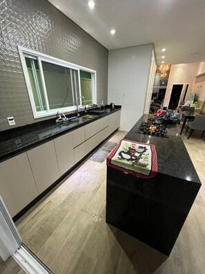 Cozinha moderna com bancada preta, uma janela e uma área de refeições visível ao fundo.