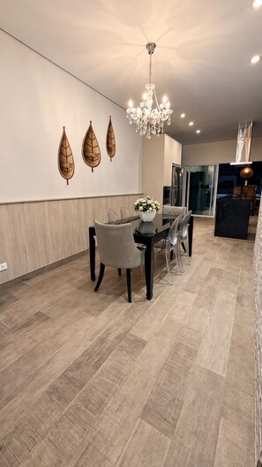 A modern dining area with a chandelier, wooden leaf wall art, and a dining table with chairs.
