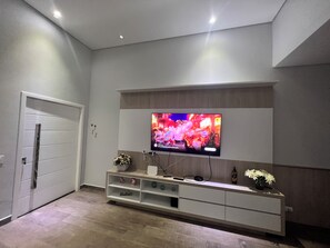 A modern living room with a flat-screen TV mounted on the wall, a white entertainment unit below, and a closed door to the left.