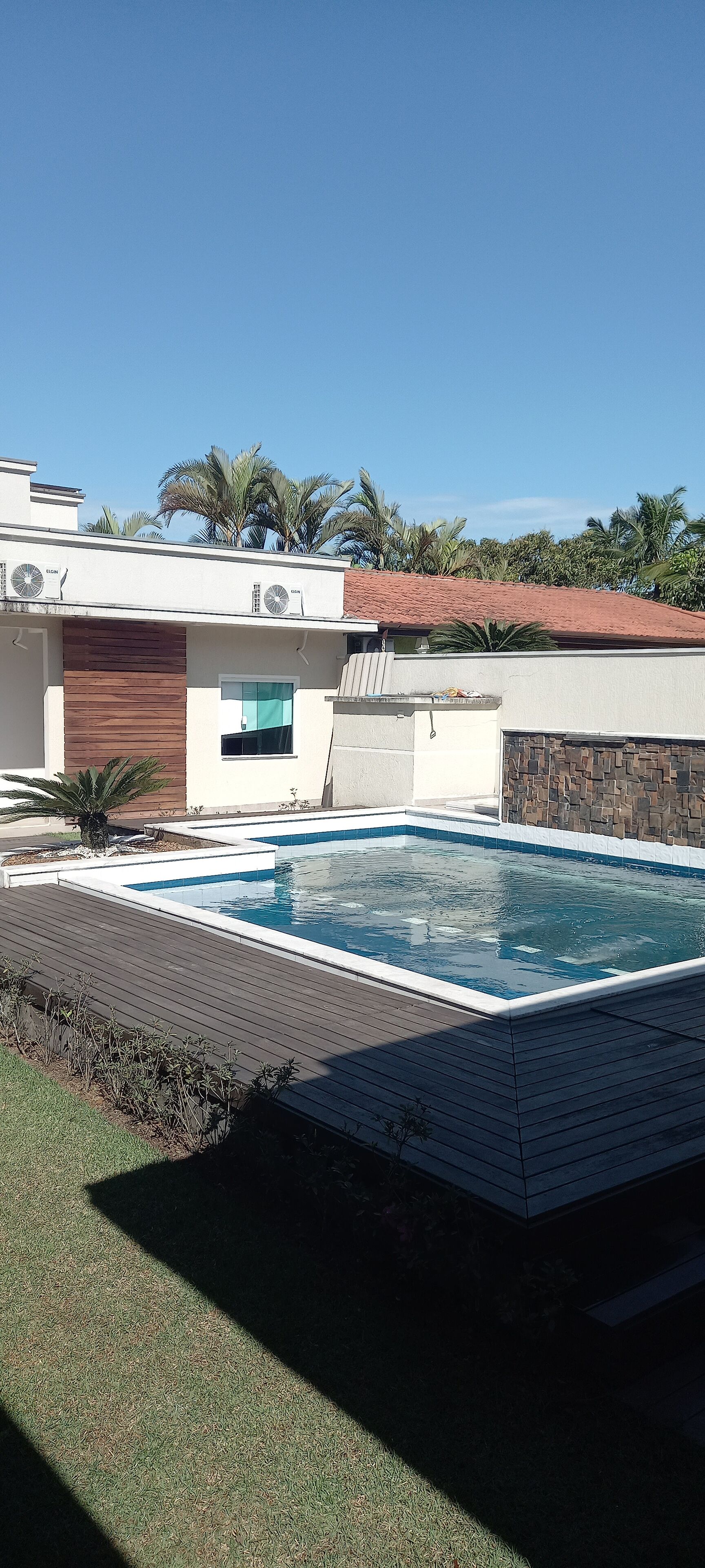 A modern house with a swimming pool, a wooden deck, and a stone wall.