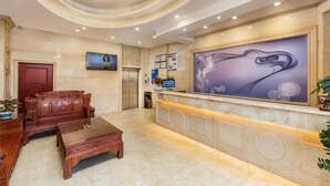 A hotel lobby with a reception desk, wooden furniture, a large wall painting, and a gold chandelier. - Nanfang Yijing Hotel (Shenzhen Baoan International Airport Gushu Subway Station store) (Shenzhen)