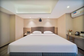 Una habitación de hotel con una cama grande, mesitas de noche, un escritorio y un aire acondicionado.