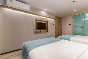 A hotel room with two beds, a TV mounted on the wall, and a glass shower door.