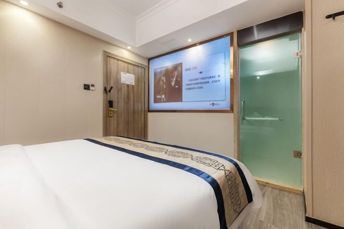 A hotel room with a bed, a television screen, and a glass shower door.