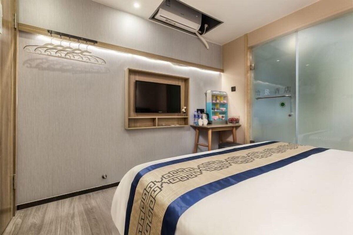 A hotel room with a bed, a TV mounted on the wall, a vending machine, and a glass door.