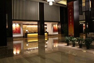 A hotel lobby with a reception desk, a large vertical banner, and potted plants.