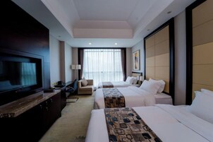 Quarto de hotel com duas camas, televisão, escrivaninha e uma janela grande com cortinas.