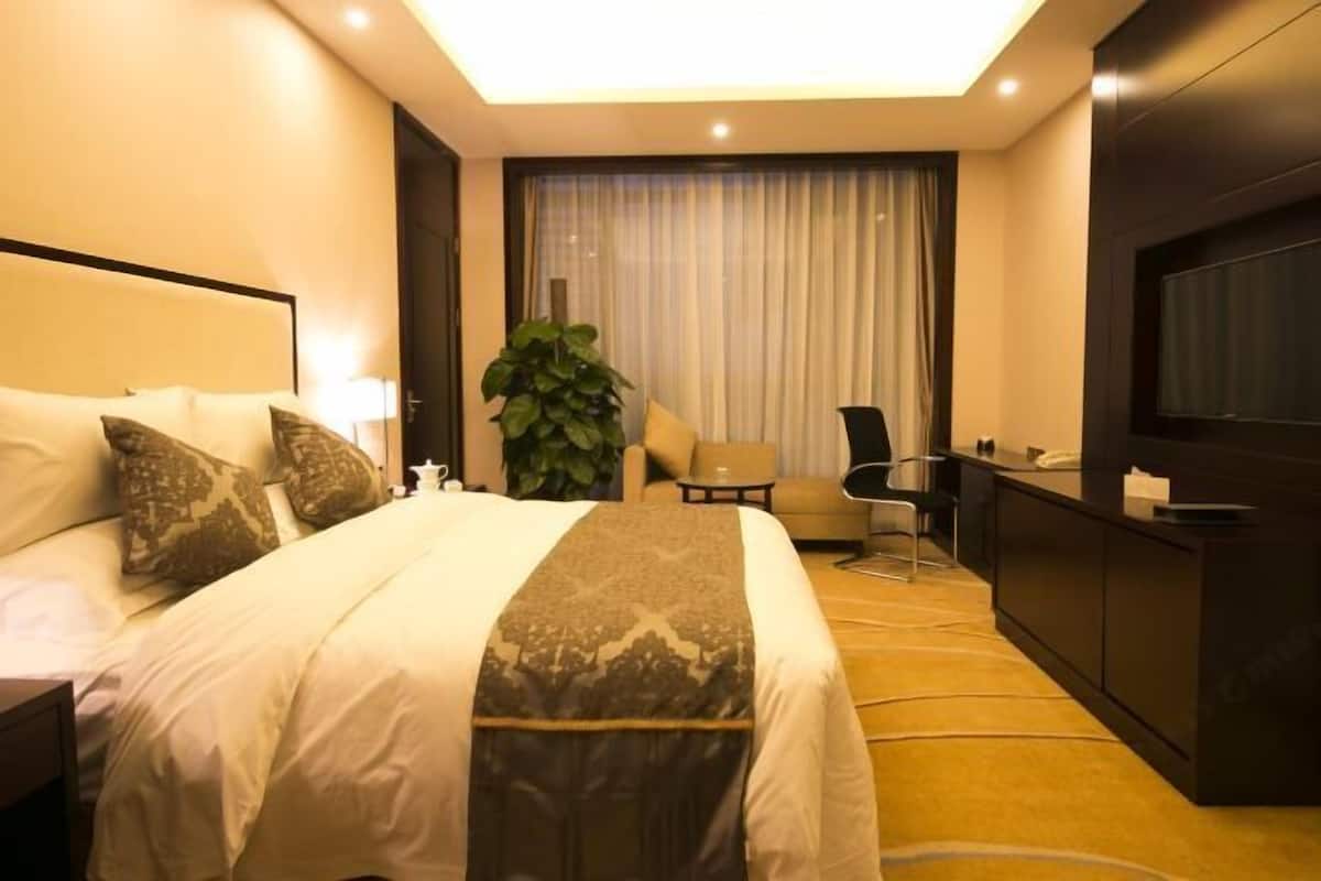 Habitación de hotel con cama, escritorio, silla, televisor y un amplio ventanal con cortinas.