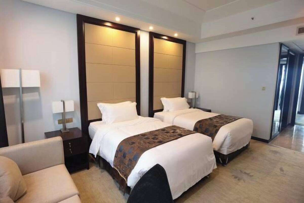 Habitación de hotel con dos camas, un sofá, una mesita de noche y un espejo grande.