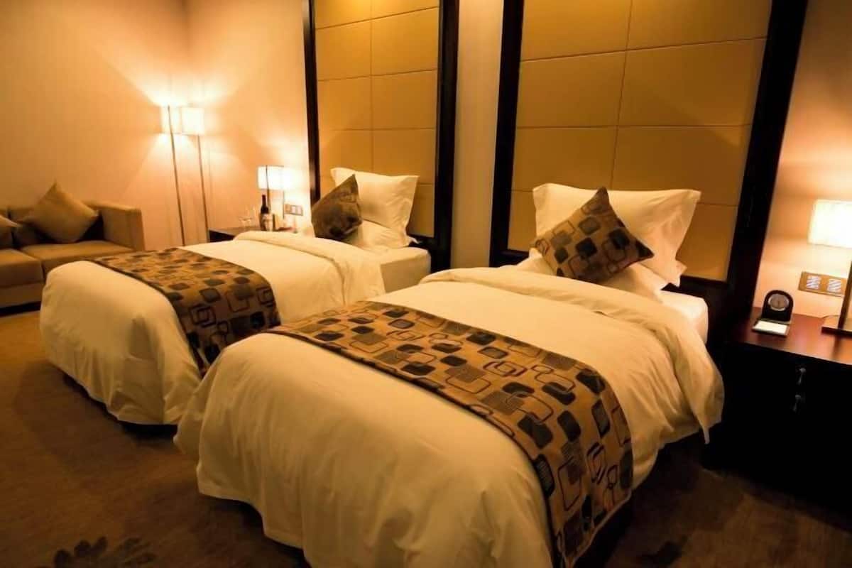 Habitación de hotel con dos camas, cada una con una manta y almohadas estampadas. A la derecha, una mesita de noche con una lámpara y un reloj.